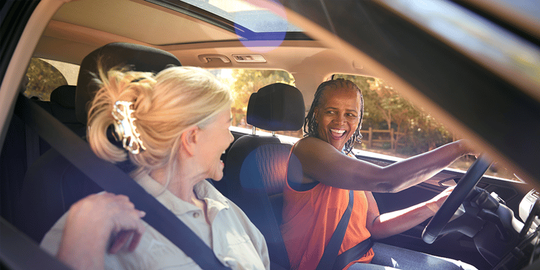 Two older women in a car smiling at each other and driving.