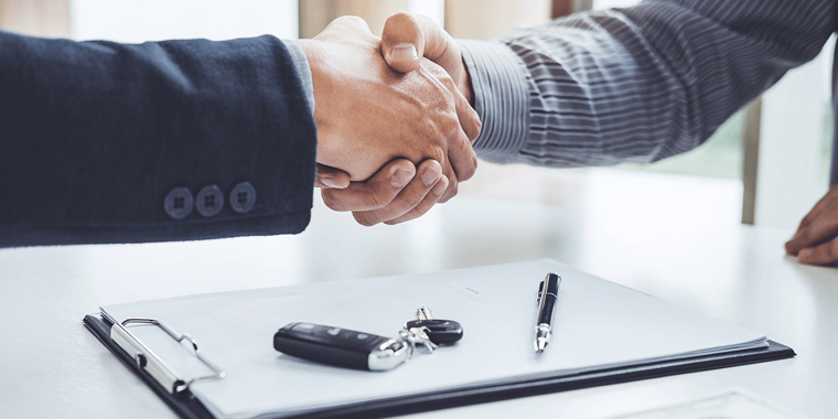 Picture of two people shaking hands over a clipboard, pen, and set of car keys as if they just closed a deal.