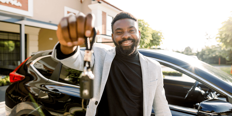 Picture of a middle-aged man smiling and holding a set of car keys in front of a car.